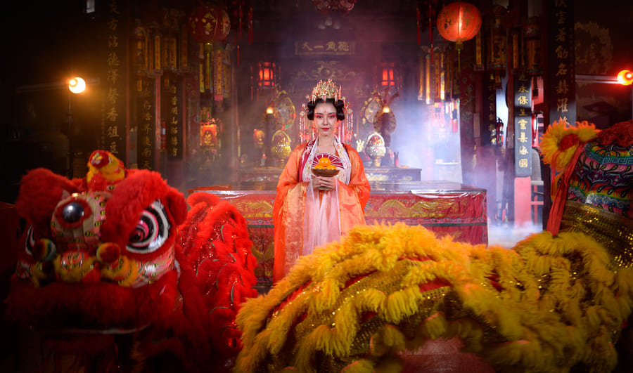 mujer frente a un altar vestida con un traje tradicional chino detrás de dos leones chinos